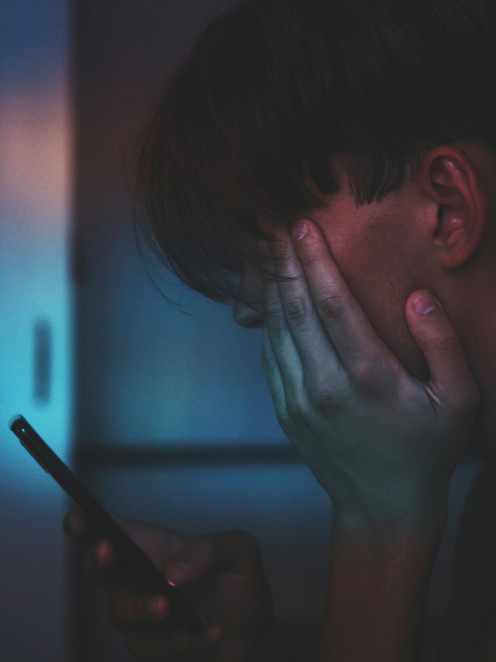 Person holding face in hand while looking at phone, showing signs of dorsal vagal shutdown and overwhelm in NYC