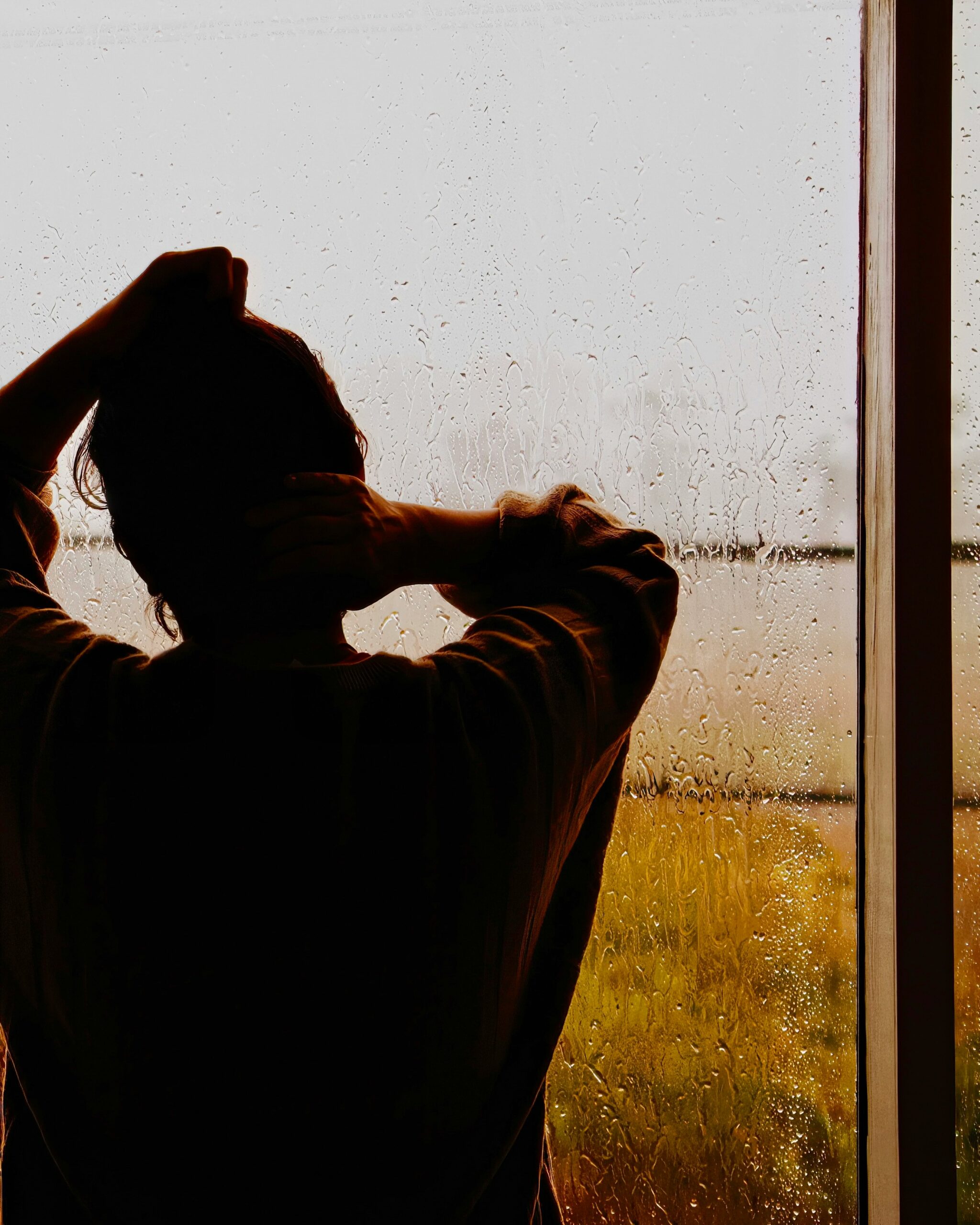Person standing by a rain-covered window reflecting on nervous system regulation in NYC somatic therapy
