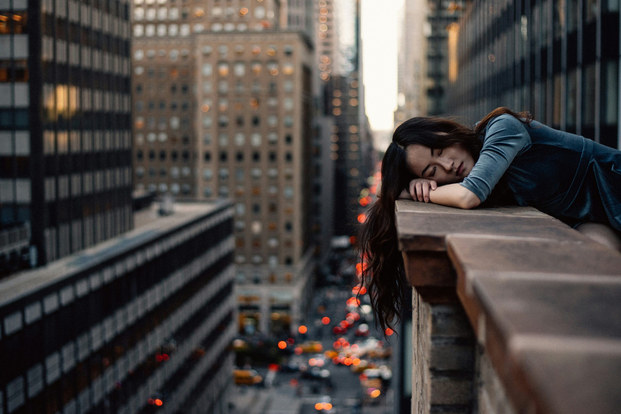 Woman resting on a rooftop ledge above New York City, symbolizing exhaustion and the need for burnout recovery through somatic therapy.