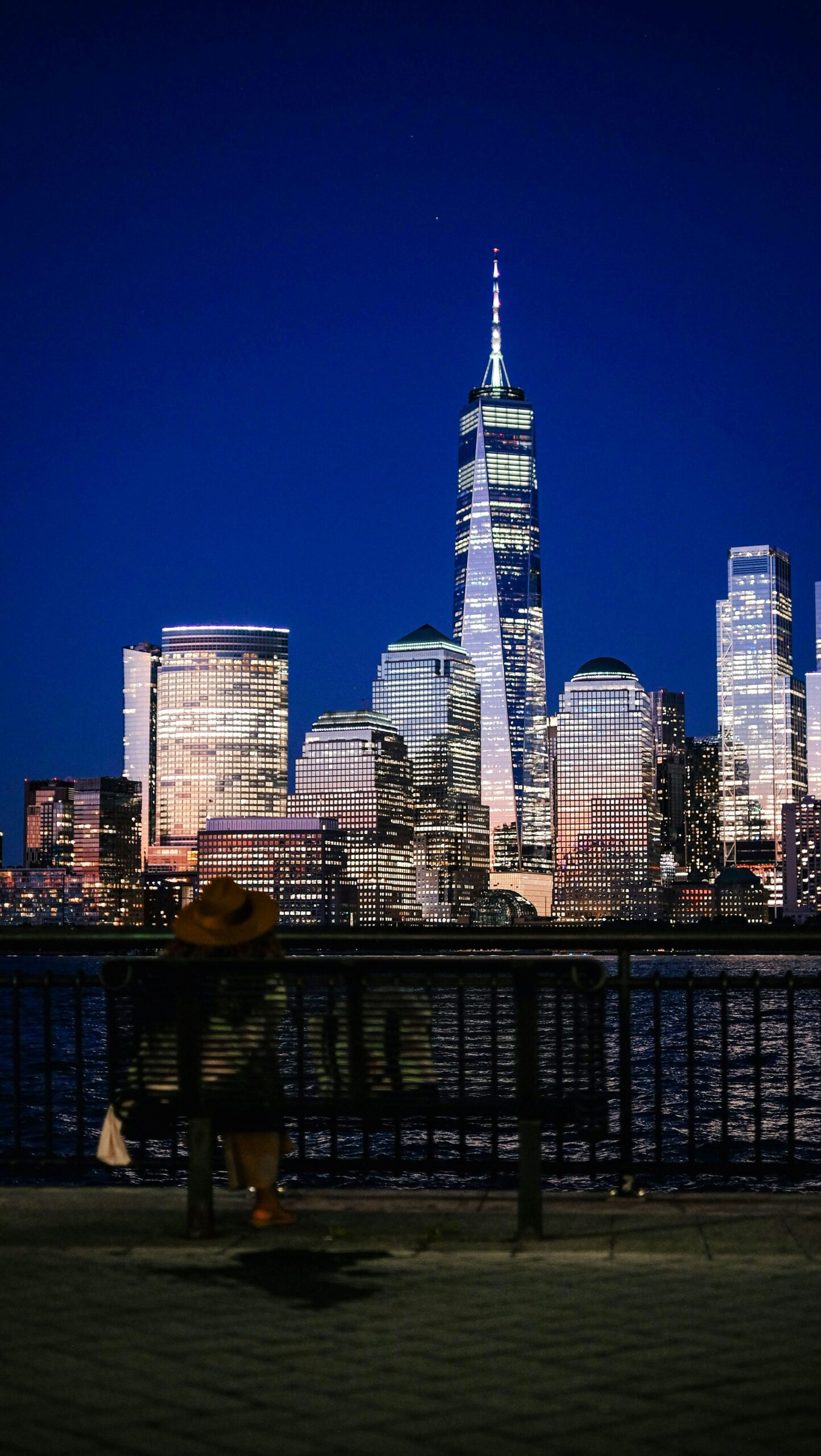 Person sitting by the water at night overlooking the New York City skyline, reflecting on healing and recovery from trauma