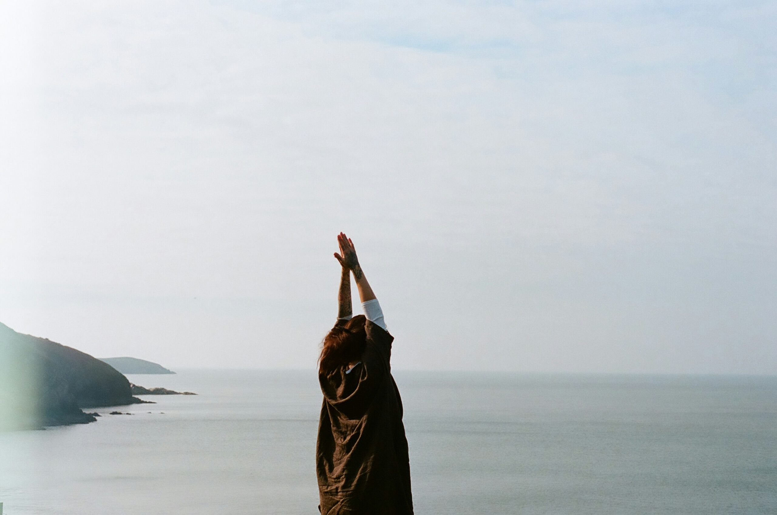 Woman raising arms toward open sky over water, representing freedom and somatic healing through body-based therapy