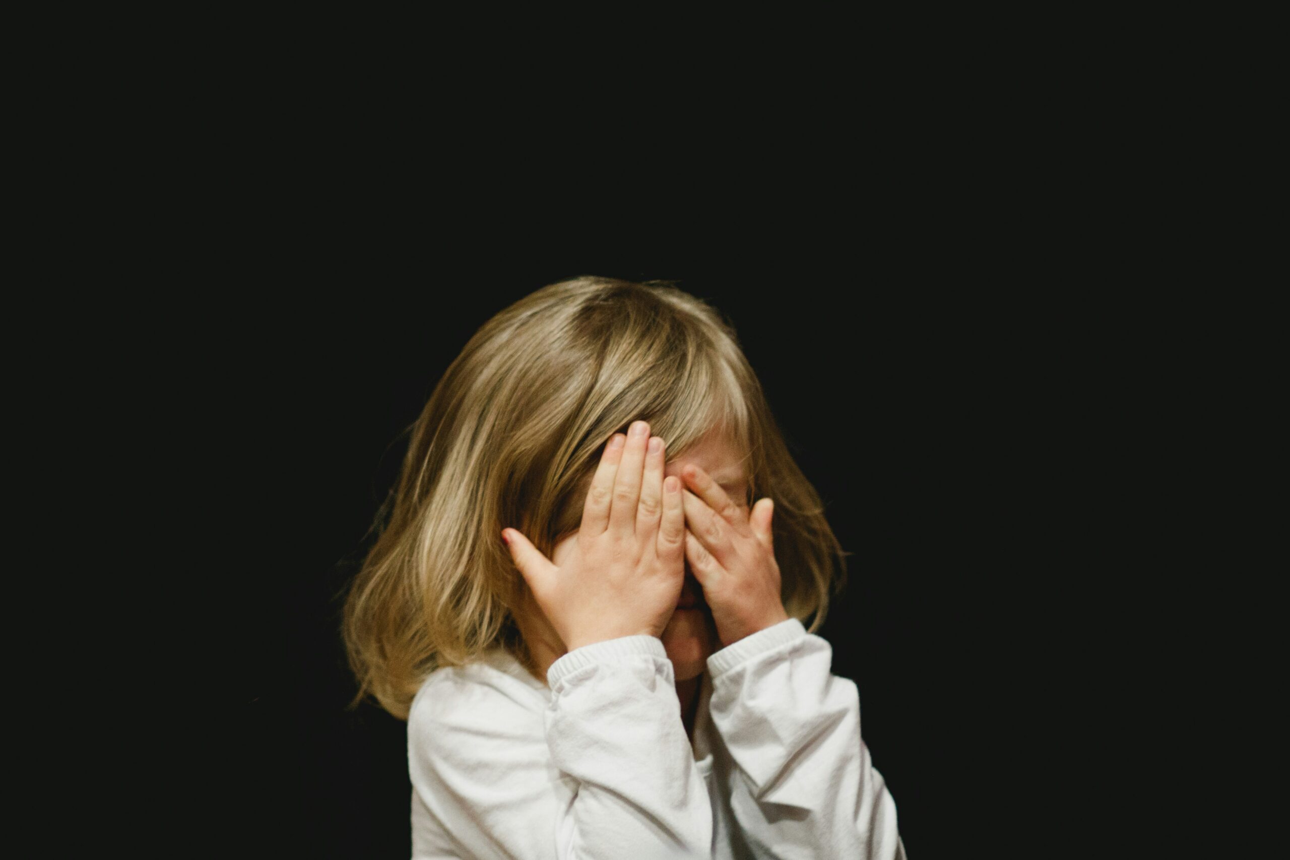 Child covering face with hands, representing emotional overwhelm addressed in childhood trauma therapy NYC